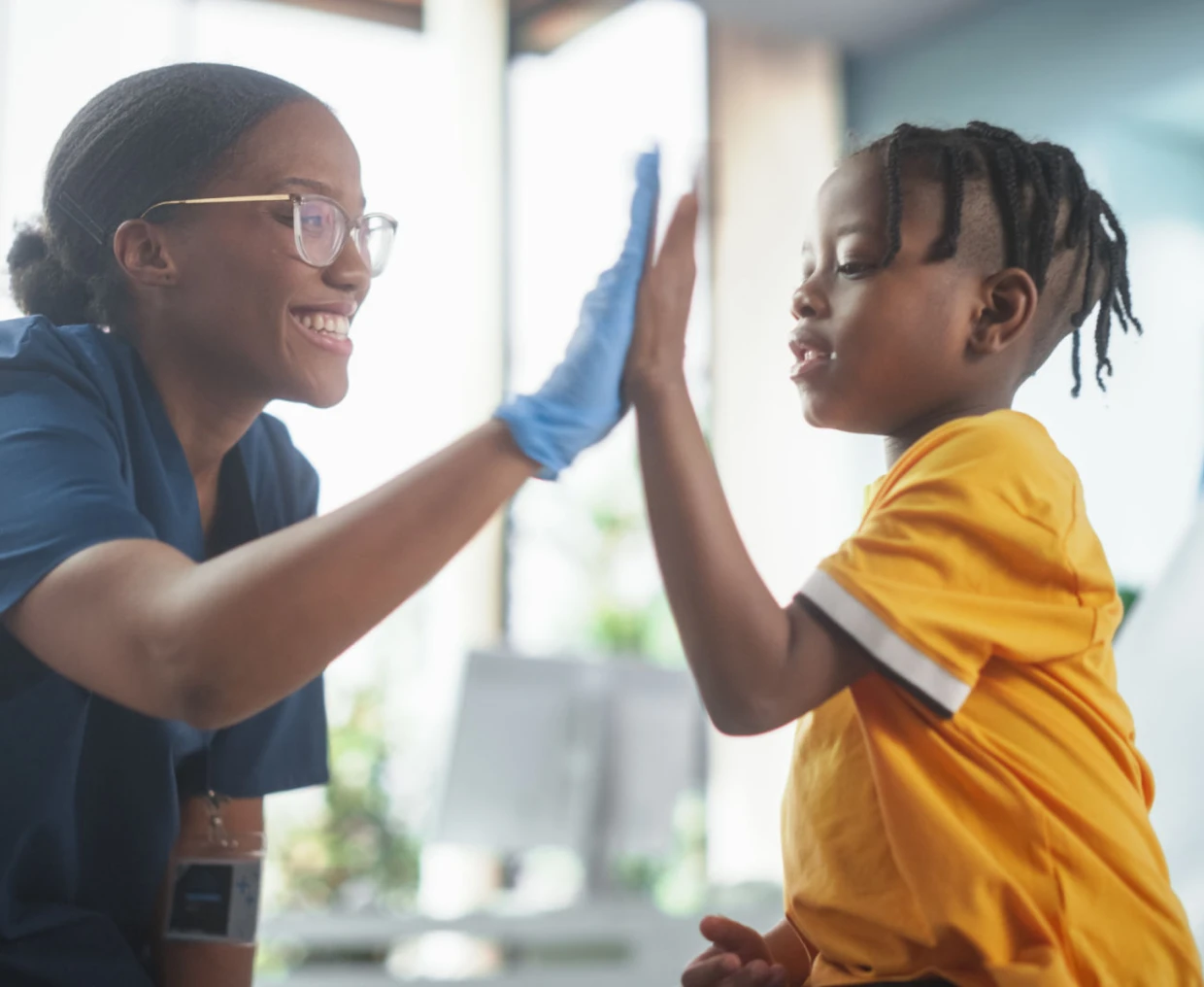 Smiling nurse high-fives young child.