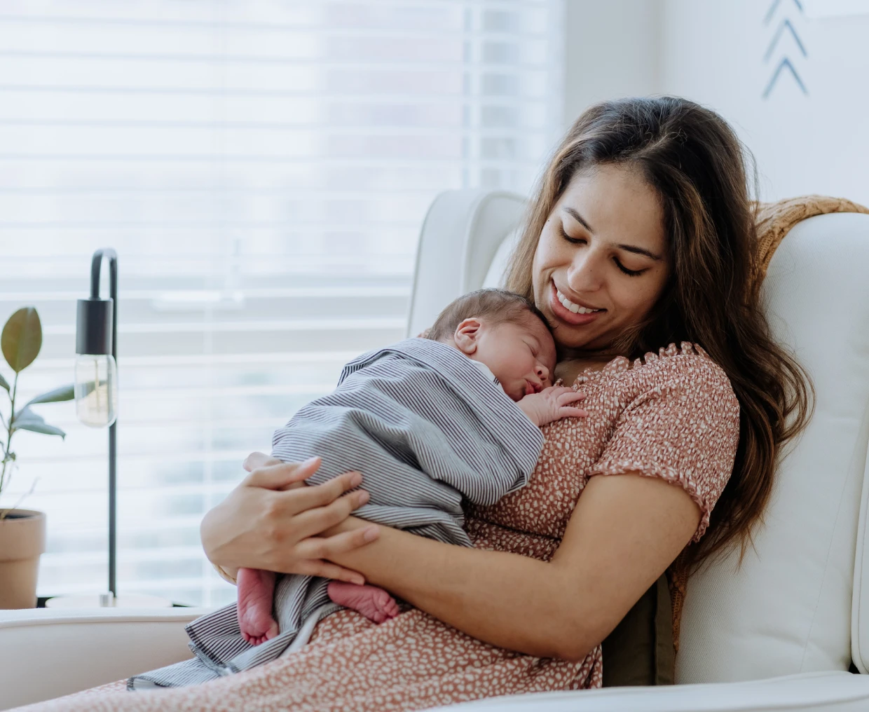 Mother holding sleeping baby in chair.