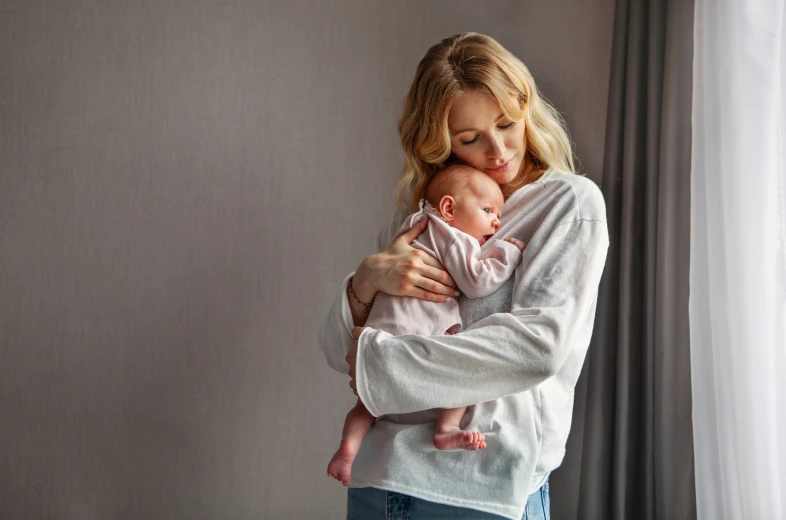 Mother cradling baby by window.